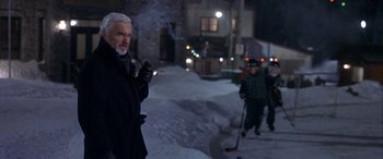 Movie still from “Mystery, Alaska” (1999), directed by Jay Roach – A man smoking a pipe while standing in the snow; Medium shot, Low angle