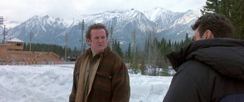 Movie still from “Mystery, Alaska” (1999), directed by Jay Roach – A man standing in front of a snowy mountain; Medium shot, Over the shoulder angle