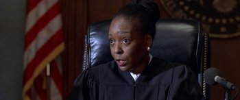 Movie still from “Mystery, Alaska” (1999), directed by Jay Roach – A woman in a black gown sitting in a black chair; Close Up shot, High angle