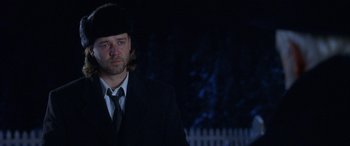 Movie still from “Mystery, Alaska” (1999), directed by Jay Roach – A man in a suit and hat standing in front of a white picket fence at night; Close Up shot, Over the shoulder angle