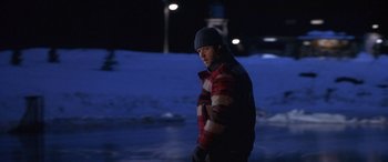 Movie still from “Mystery, Alaska” (1999), directed by Jay Roach – A man standing in the snow at night wearing winter clothing; Medium shot, Over the shoulder angle
