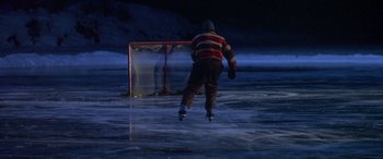Movie still from “Mystery, Alaska” (1999), directed by Jay Roach – A man is playing ice hockey on a frozen lake at night; Wide shot, High angle
