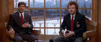 Movie still from “Mystery, Alaska” (1999), directed by Jay Roach – Two men sitting in front of a large window with a view of an ice rink in the background; Medium shot, High angle