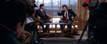 Movie still from “Mystery, Alaska” (1999), directed by Jay Roach – Two men in suits and ties sitting in front of a window; Medium shot, High angle