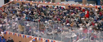 Movie still from “Mystery, Alaska” (1999), directed by Jay Roach – A group of people sitting in a stadium holding newspapers; Extreme Wide shot, High angle