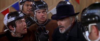 Movie still from “Mystery, Alaska” (1999), directed by Jay Roach – A man wearing a hat and a suit and a hockey uniform; Close Up shot, Over the shoulder angle