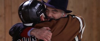 Movie still from “Mystery, Alaska” (1999), directed by Jay Roach – An older man in a black hat hugging another older man; Close Up shot, High angle