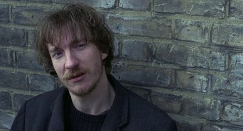 Movie still from “Naked” (1993), directed by Mike Leigh – A person wearing a jacket near a brick wall; Close Up shot, Over the shoulder angle