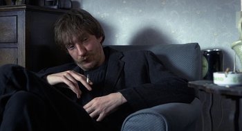 Movie still from “Naked” (1993), directed by Mike Leigh – A man sitting on a couch smoking a cigarette; Medium shot, High angle