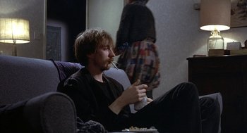 Movie still from “Naked” (1993), directed by Mike Leigh – A man sitting in a chair with a cigarette in his mouth; Medium shot, High angle