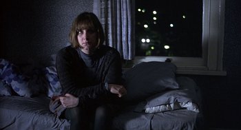 Movie still from “Naked” (1993), directed by Mike Leigh – A woman sitting on a bed in front of a window at night; Medium shot, High angle