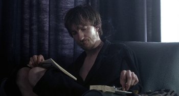 Movie still from “Naked” (1993), directed by Mike Leigh – A man sitting in a chair reading a book; Close Up shot, Over the shoulder angle