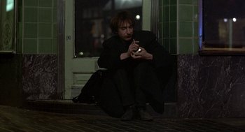 Movie still from “Naked” (1993), directed by Mike Leigh – A man sitting on the ground while holding a cell phone; Medium shot, Low angle