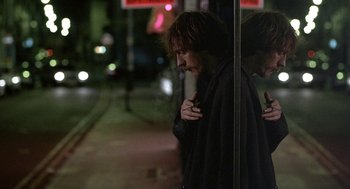 Movie still from “Naked” (1993), directed by Mike Leigh – A man standing in front of a window at night; Medium shot, Over the shoulder angle