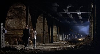 Movie still from “Naked” (1993), directed by Mike Leigh – A group of people standing in an abandoned building; Extreme Wide shot, High angle