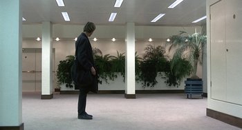 Movie still from “Naked” (1993), directed by Mike Leigh – A person standing in a room with plants; Wide shot, High angle