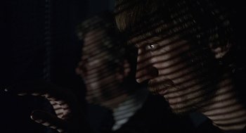 Movie still from “Naked” (1993), directed by Mike Leigh – A man is looking at the camera through the blinds of a window; Close Up shot, Over the shoulder angle