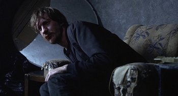 Movie still from “Naked” (1993), directed by Mike Leigh – A man sitting on a couch in a room; Medium shot, Low angle