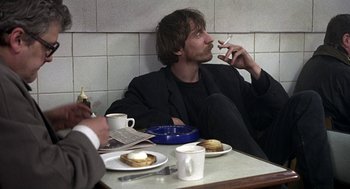 Movie still from “Naked” (1993), directed by Mike Leigh – A man sitting in front of a plate of food; Medium shot, Over the shoulder angle