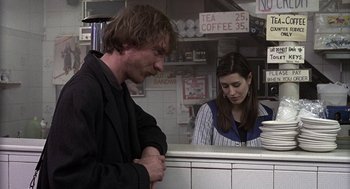 Movie still from “Naked” (1993), directed by Mike Leigh – A man and a woman are standing at a counter in a restaurant; Medium shot, Over the shoulder angle