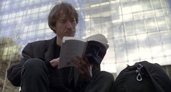 Movie still from “Naked” (1993), directed by Mike Leigh – A man reading a book while sitting in a chair; Medium shot, Low angle