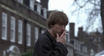 Movie still from “Naked” (1993), directed by Mike Leigh – A man smoking a cigarette in front of a brick building; Close Up shot, Low angle