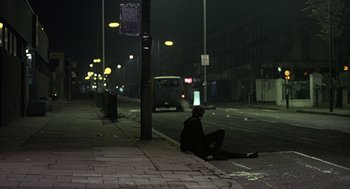 Movie still from “Naked” (1993), directed by Mike Leigh – A man sitting on the side of the street at night; Wide shot, Low angle