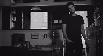 Movie still from “Frances Ha” (2012), directed by Noah Baumbach – A black and white photo of a man standing in front of a table; Medium shot, Low angle