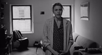 Movie still from “Frances Ha” (2012), directed by Noah Baumbach – A black and white photo of a woman standing in front of a window; Medium shot, Over the shoulder angle