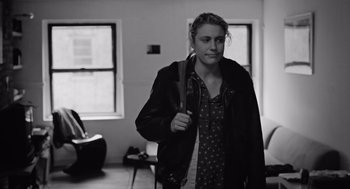 Movie still from “Frances Ha” (2012), directed by Noah Baumbach – A woman holding a tennis racquet while standing in a room; Medium shot, Over the shoulder angle