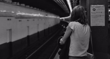 Movie still from “Frances Ha” (2012), directed by Noah Baumbach – A woman standing on a train platform waiting for a train to arrive; Medium shot, Low angle