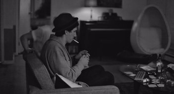 Movie still from “Frances Ha” (2012), directed by Noah Baumbach – A man sitting in a chair smoking a cigarette; Medium shot, High angle