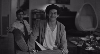 Movie still from “Frances Ha” (2012), directed by Noah Baumbach – A man sitting on a couch holding a book; Medium shot, Over the shoulder angle