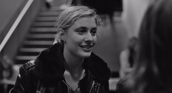 Movie still from “Frances Ha” (2012), directed by Noah Baumbach – A young woman smiles for the camera while sitting on some steps; Close Up shot, Over the shoulder angle