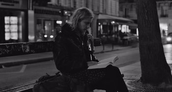 Movie still from “Frances Ha” (2012), directed by Noah Baumbach – A woman sitting on the side of the street reading a book; Medium shot, Low angle