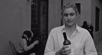 Movie still from “Frances Ha” (2012), directed by Noah Baumbach – A woman is holding a bottle of wine while another woman is sitting on a bench; Close Up shot, Over the shoulder angle