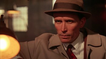 Movie still from “Naked Lunch” (1991), directed by David Cronenberg – A person wearing a hat and a suit; Close Up shot, High angle