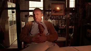 Movie still from “Naked Lunch” (1991), directed by David Cronenberg – A man sitting in a chair wearing a tie; Medium shot, Low angle