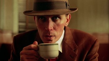 Movie still from “Naked Lunch” (1991), directed by David Cronenberg – A man in a hat drinking a cup of coffee; Close Up shot, Low angle