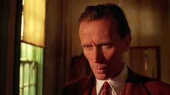 Movie still from “Naked Lunch” (1991), directed by David Cronenberg – A person wearing a suit and tie; Close Up shot, Low angle