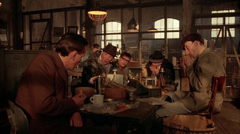 Movie still from “Naked Lunch” (1991), directed by David Cronenberg – A group of people sitting around a table in a room; Wide shot, Over the shoulder angle