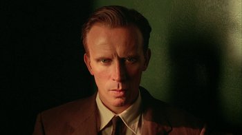 Movie still from “Naked Lunch” (1991), directed by David Cronenberg – A person wearing a suit and tie; Close Up shot, Low angle