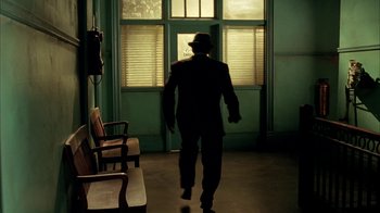 Movie still from “Naked Lunch” (1991), directed by David Cronenberg – A man in a suit and hat walking in a room; Wide shot, Low angle