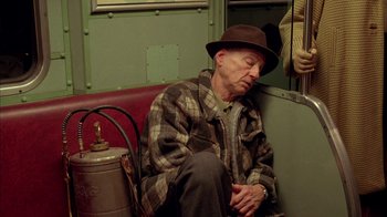 Movie still from “Naked Lunch” (1991), directed by David Cronenberg – An older man sitting on a bench next to a fire hydrant; Medium shot, High angle