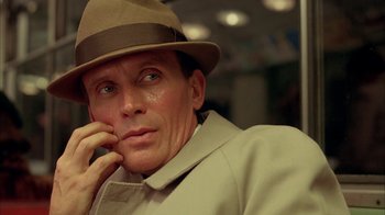 Movie still from “Naked Lunch” (1991), directed by David Cronenberg – A person wearing a hat and holding a cell phone to his ear; Close Up shot, Low angle