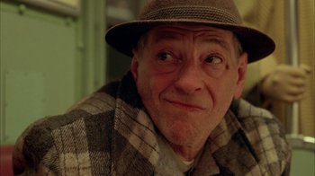 Movie still from “Naked Lunch” (1991), directed by David Cronenberg – An older man wearing a hat and a plaid jacket; Close Up shot, Low angle