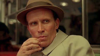 Movie still from “Naked Lunch” (1991), directed by David Cronenberg – A person wearing a hat and holding his hand to his face; Close Up shot, Low angle