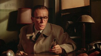 Movie still from “Naked Lunch” (1991), directed by David Cronenberg – A man sitting at a table holding a cell phone; Close Up shot, Low angle