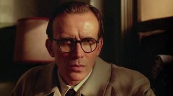 Movie still from “Naked Lunch” (1991), directed by David Cronenberg – A person wearing a suit and glasses; Close Up shot, Low angle