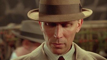Movie still from “Naked Lunch” (1991), directed by David Cronenberg – A person wearing a suit and a hat; Close Up shot, Low angle